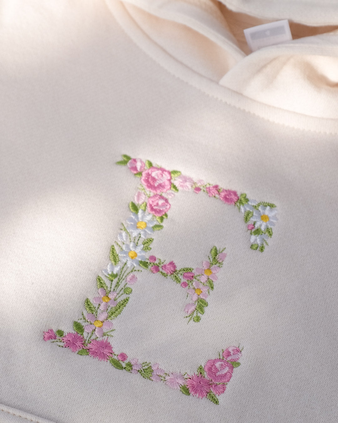 Uppercase E embroidered using floral design in pastel pink